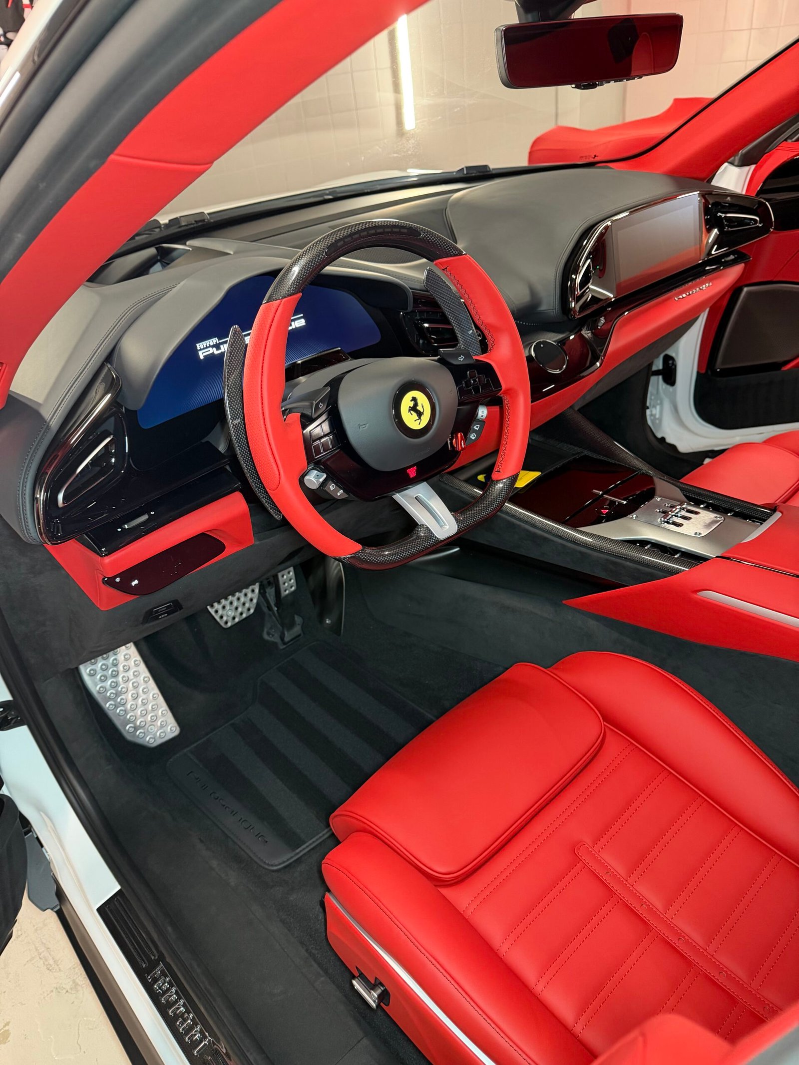Volant et planche de bord d'une Ferrari Purosangue, sellerie cuir rouge et inscription Purosangue visible sur la console centrale