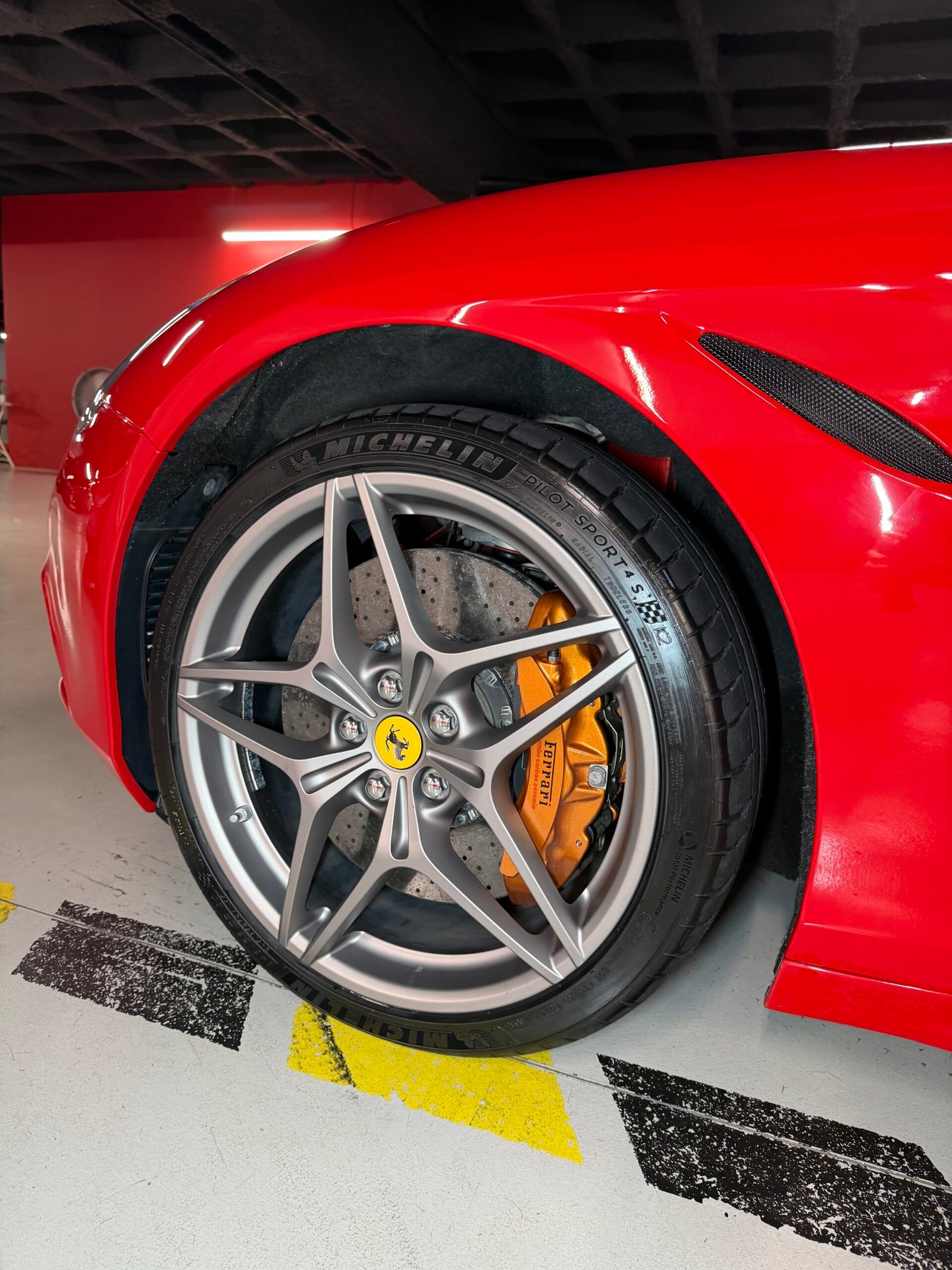 Détail d'une jante et d'un étrier de frein orange sur une Ferrari rouge, dans un parking souterrain