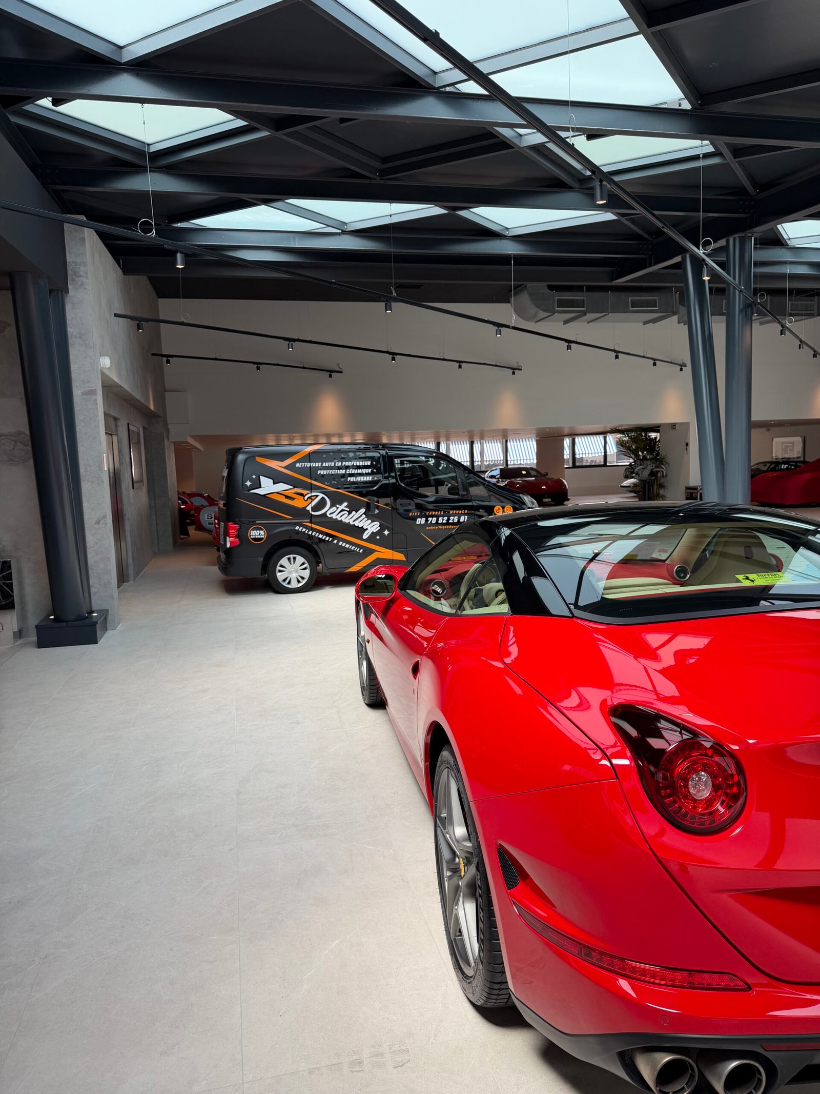Ferrari rouge cabriolet vue de trois-quarts arrière dans le showroom YS Detailing, fourgon d'intervention visible en arrière-plan