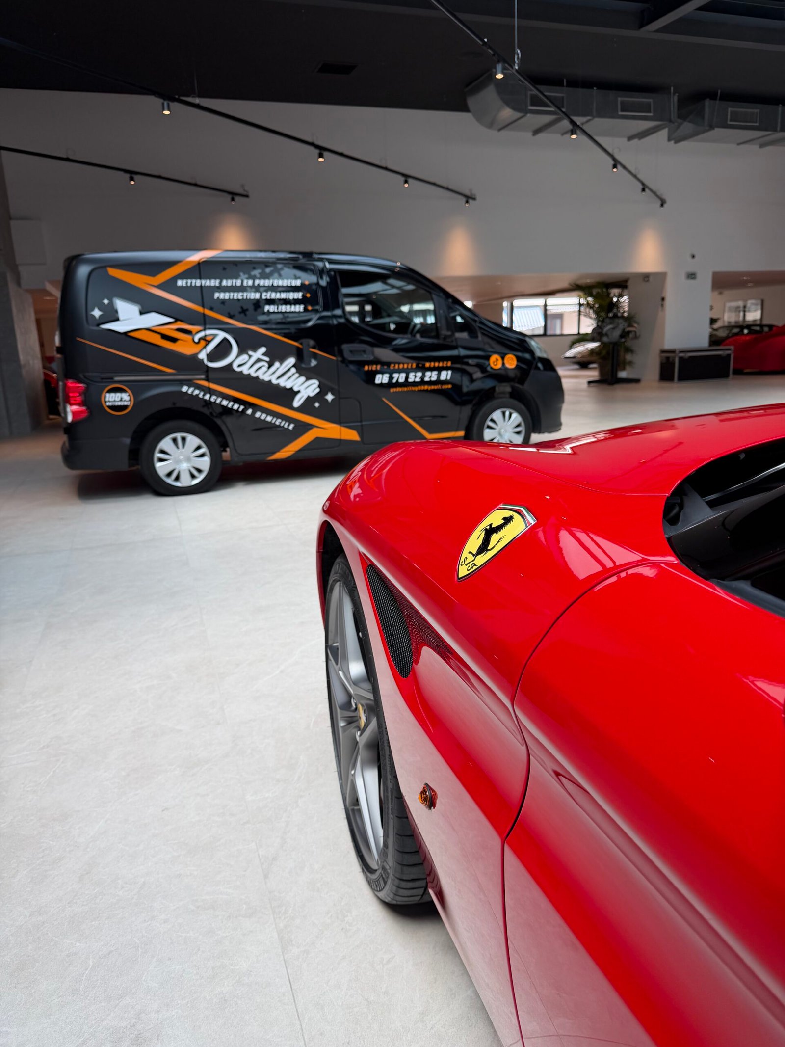Ferrari rouge, écusson et aile avant en premier plan, showroom YS Detailing avec fourgon d'intervention en arrière-plan